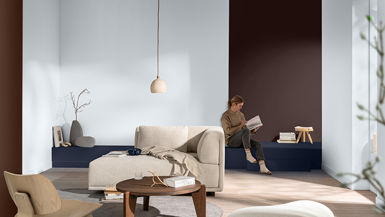 On the left there are painted balls in the back of a canvas with objects from around the world. On the right brown coloured wall with white sofa with boy walking in the living room 
